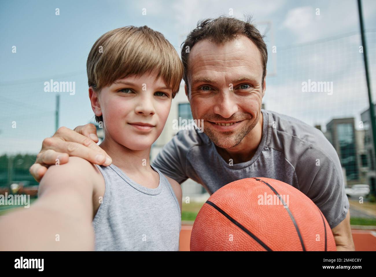 POV di padre e figlio che prendono selfie in campo da basket e che godono di sport insieme Foto Stock