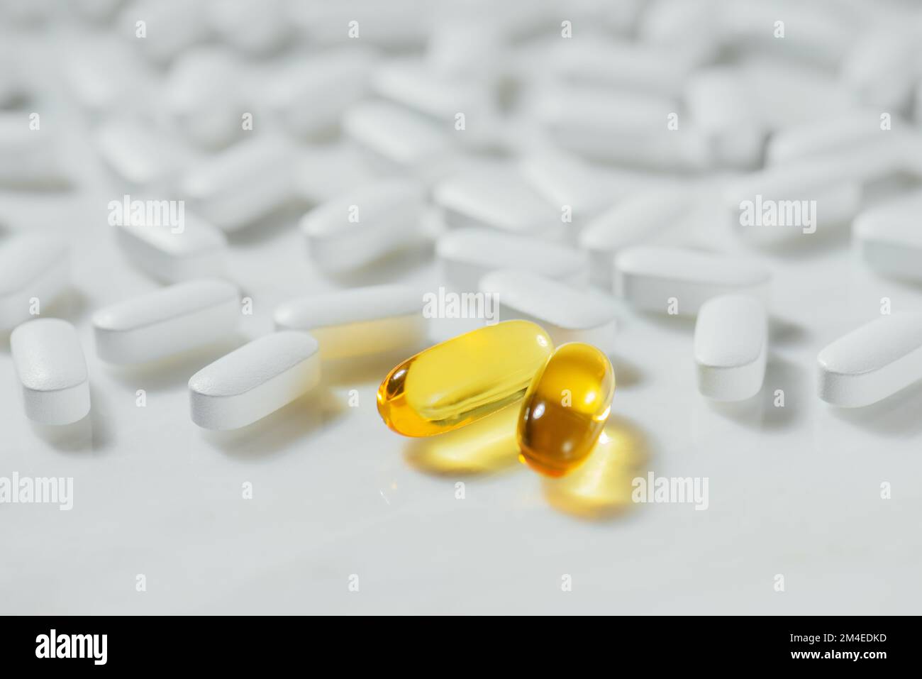 Compresse bianche con una capsula d'oro giallo che si distingue dagli altri contro sfondi di marmo bianco, concetto di alimentazione sana, pillole Foto Stock