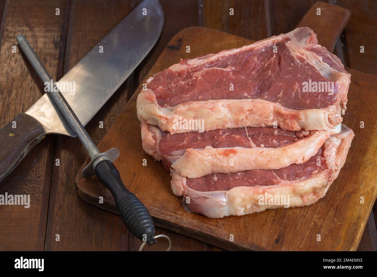 Bistecche argentine crude su un tagliere di legno con coltello e acciaio per affilatura. Foto Stock