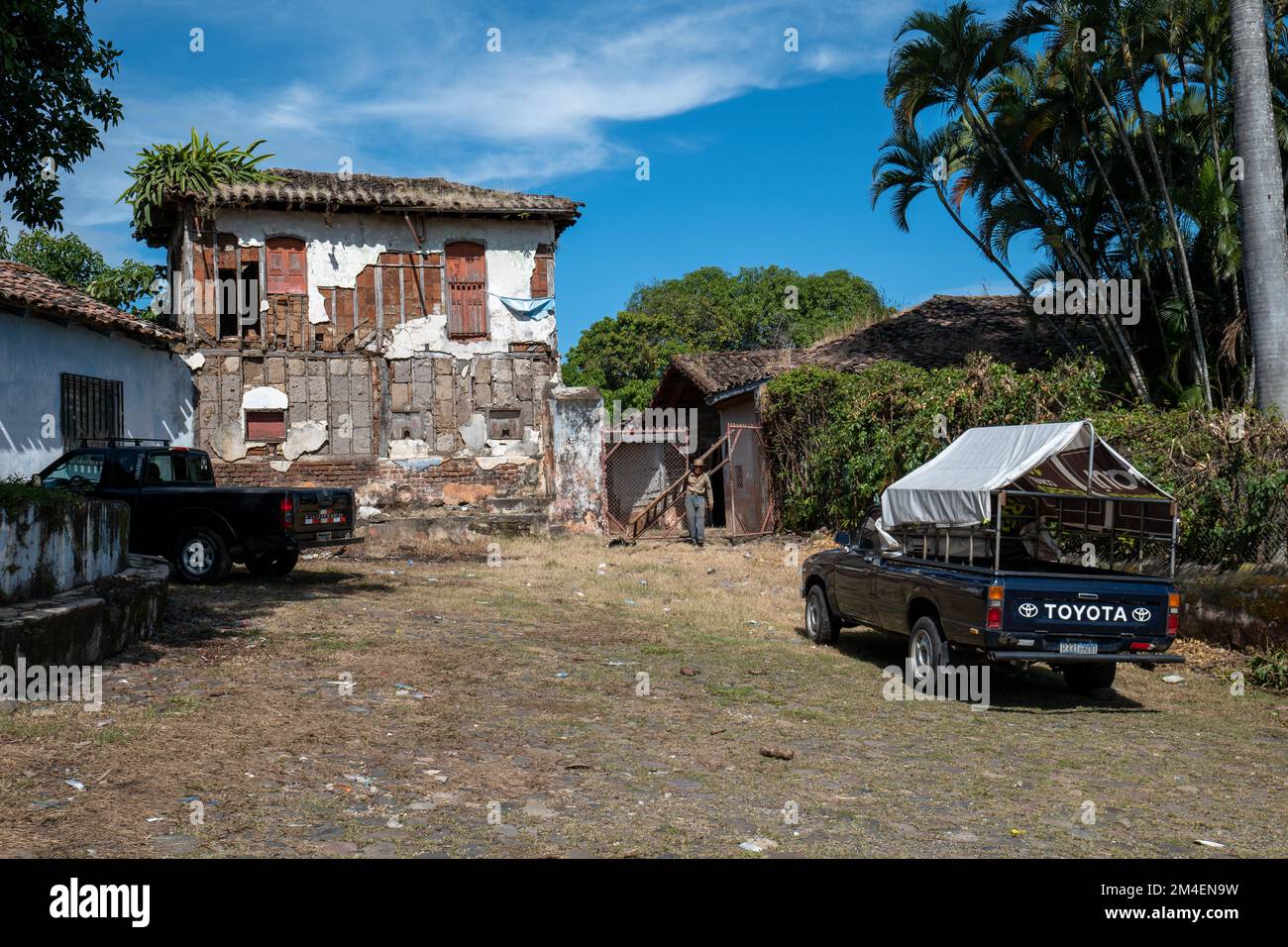La Labor, la Libertad, Salvador - 27 ottobre 2022 - Un uomo Salvadoran si trova accanto a una porta arrugginita di fronte a un camioncino in una sterrata Foto Stock