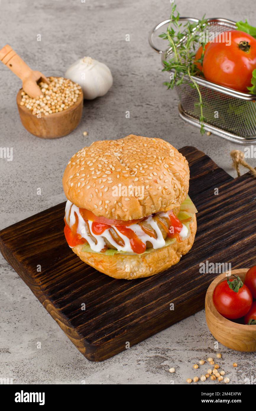 Hamburger fatti in casa con manzo, cipolla, pomodoro, lattuga e formaggio. Hamburger fresco primo piano su tavolo rustico in legno con patatine fritte e patatine fritte. Foto Stock