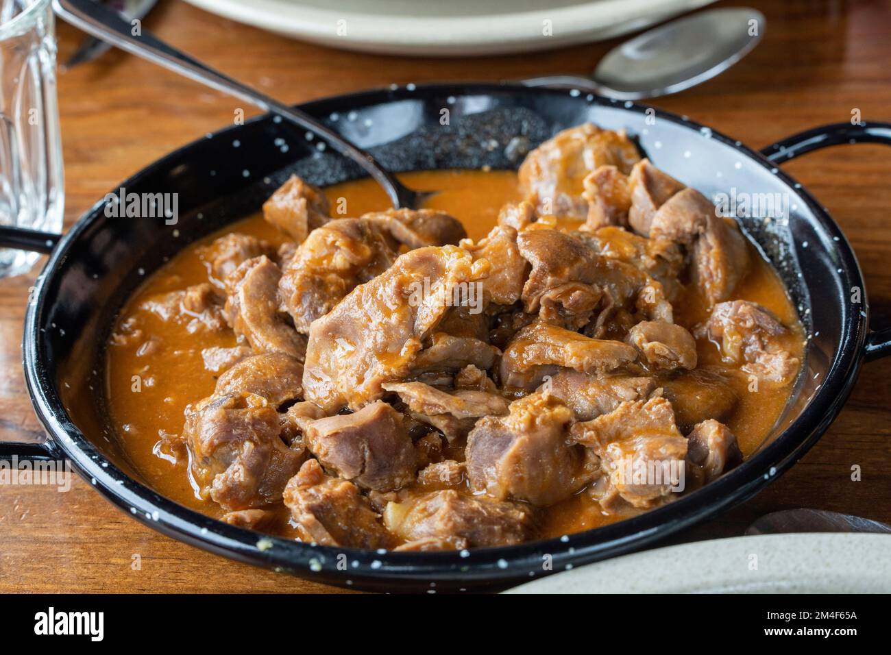 Piatto tradizionale portoghese Moelas - gizzard di pollo stufato servito in una padella nera con salsa ricca Foto Stock