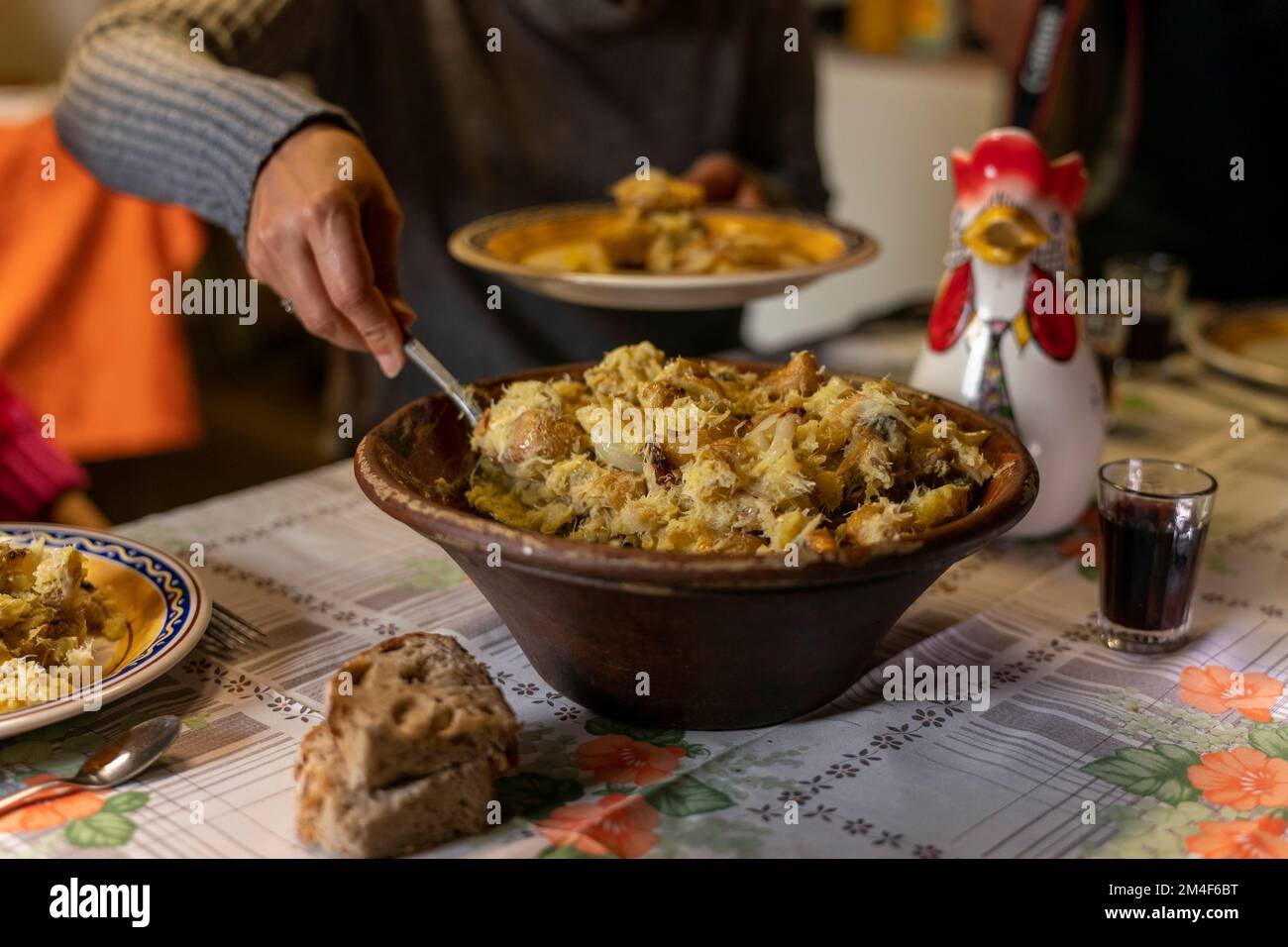 Persona che serve un tipico piatto portoghese con pesce merluzzo, olio d'oliva e patate servito in una pentola di argilla su un tradizionale tavolo da pranzo rustico Foto Stock