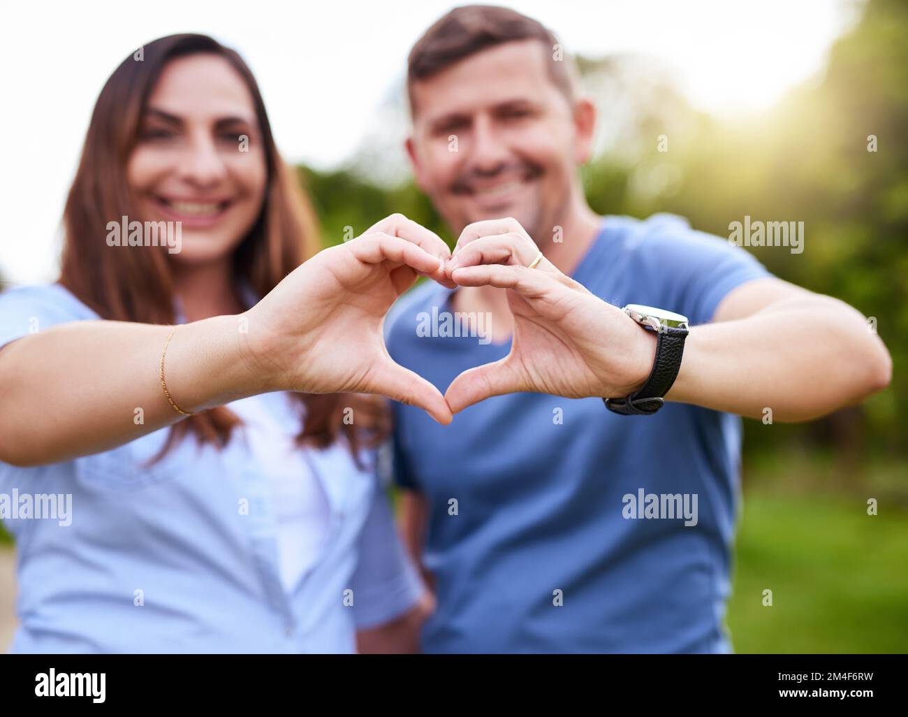 Il nostro amore prospera. Ritratto di una giovane coppia allegra che forma un cuore con le mani mentre si trova all'esterno in un parco durante il giorno. Foto Stock