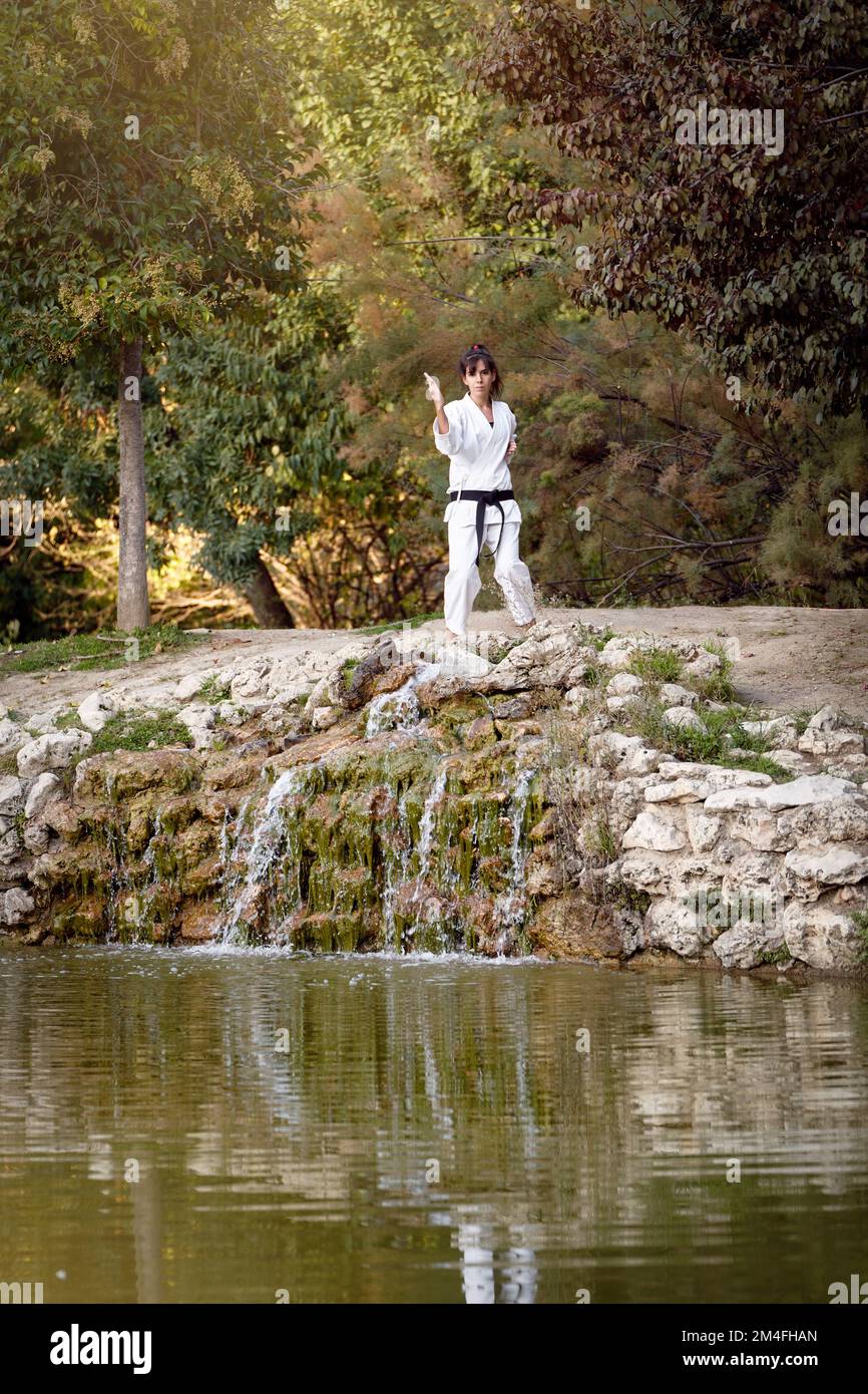 Donna in kimono bianco con cintura nera che guarda la macchina fotografica mentre si allenano karate all'aperto nella natura. Concetto di sport e arti marziali. Foto Stock