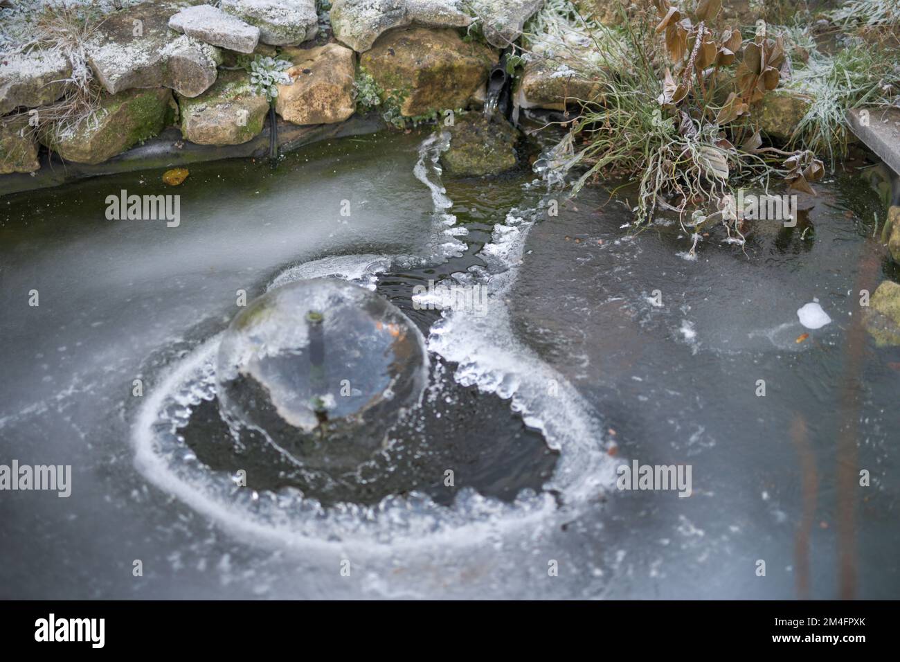 Un laghetto giardino coperto di ghiaccio con un foro per la fontana d'acqua, scena inverni Foto Stock