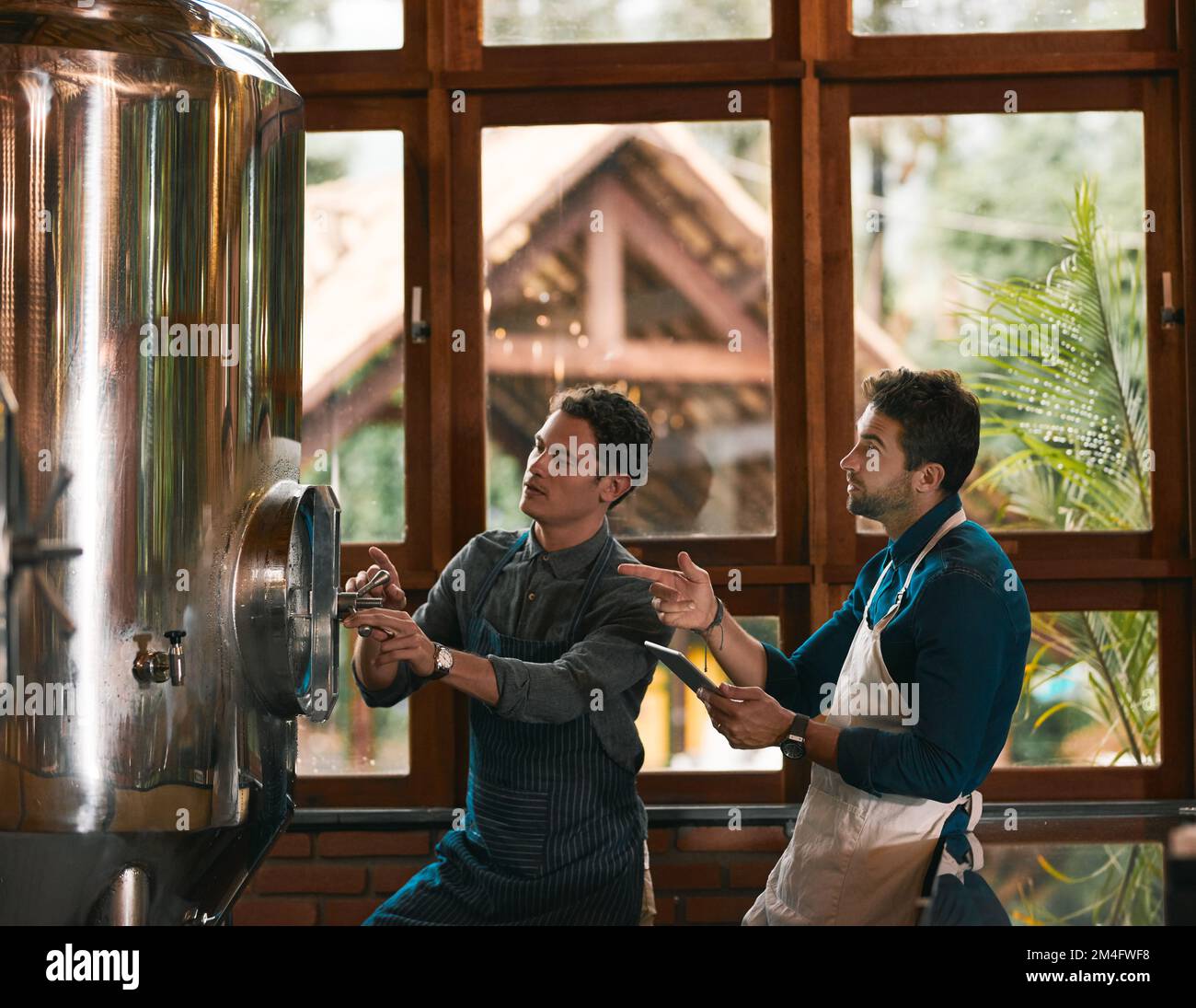 Assicurarsi che tutto funzioni correttamente. due giovani lavoratori che ispezionano i loro macchinari per la produzione della birra all'interno di una birreria durante il Foto Stock