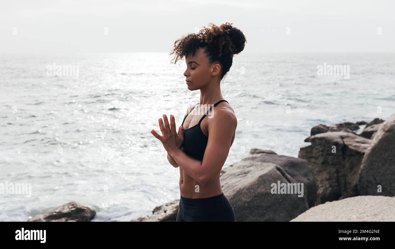 Donna in abbigliamento sportivo meditando all'aperto all'oceano Foto Stock