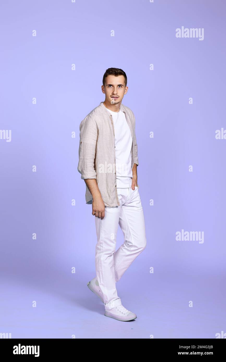 uomo caucasico in casual abiti bianchi posati su sfondo viola pastello. Foto a lunghezza intera Foto Stock