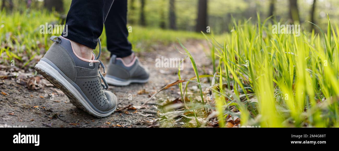 Scarpe sportive a piedi sul sentiero nella foresta. Donna che si arrampica nel bosco in primavera. Vista panoramica Foto Stock