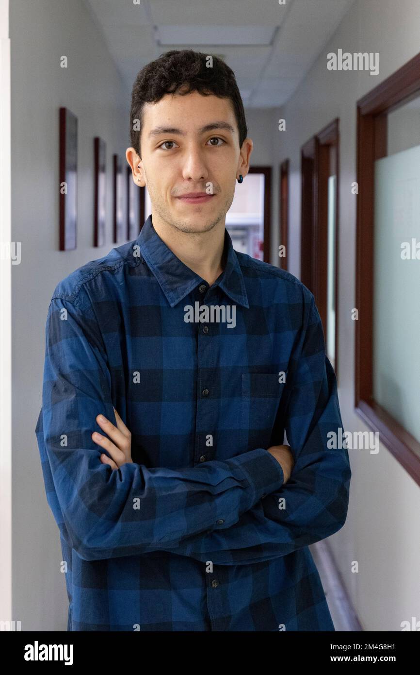 Ritratto di un giovane caucasico sorridente con le mani incrociate in un lungo corridoio che indossa una camicia a quadri blu e nera. Fotografia di ritratti. Modello Foto Stock