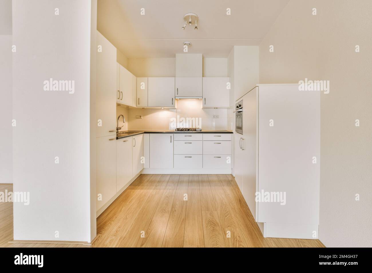 una cucina con armadi bianchi e pavimento in legno nel mezzo della stanza, che guarda alla zona pranzo Foto Stock