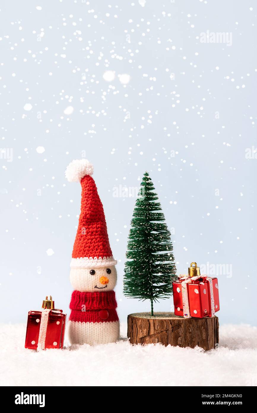 La fiaba di Natale composizione di un pupazzo di neve lavorato a maglia in un cappello e un maglione di Babbo Natale. Piccolo albero di Natale con due regali rossi Foto Stock