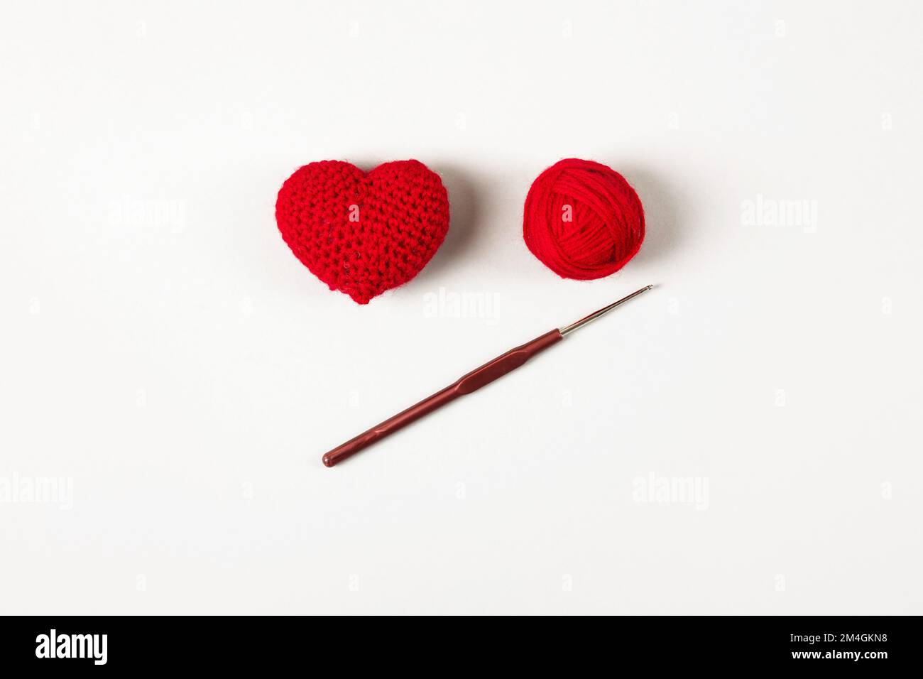 Cuore rosso arroccato su fondo grigio e una palla di filo con un gancio. San Valentino, simbolo dell'amore. Foto Stock