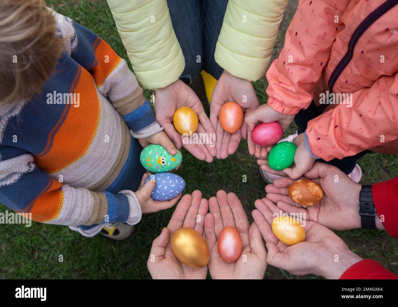 Mani di 5 persone, bambini e adulti, tenere colorate uova di Pasqua in cerchio. Nessuna faccia. Vista dall'alto . Tradizione di vacanza familiare a Pasqua. Venerdì Foto Stock
