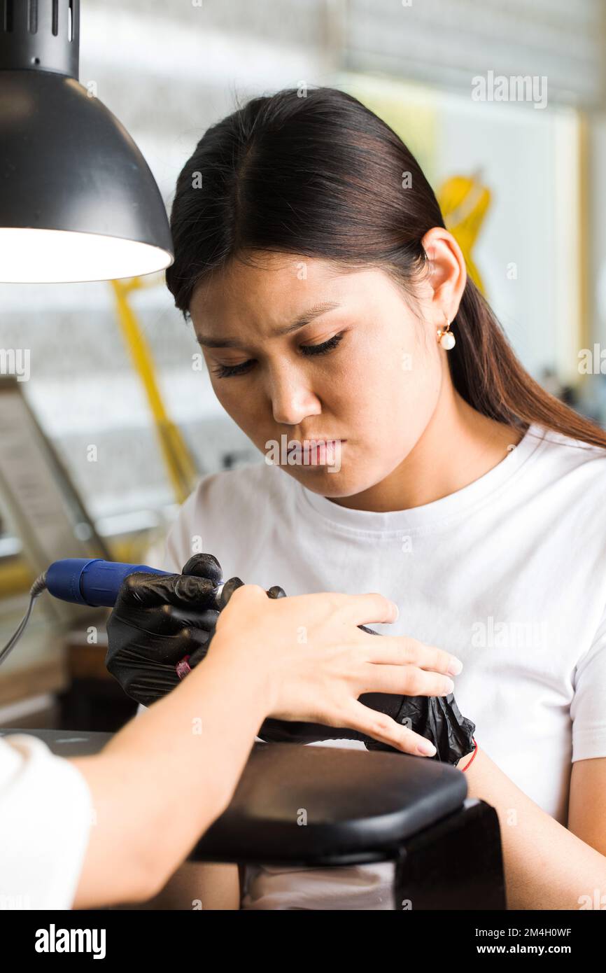 Manicure hardware. Processo di concimazione, rimozione della cuticola con un taglierino. Unghie di lavorazione con una lima elettrica. Foto Stock