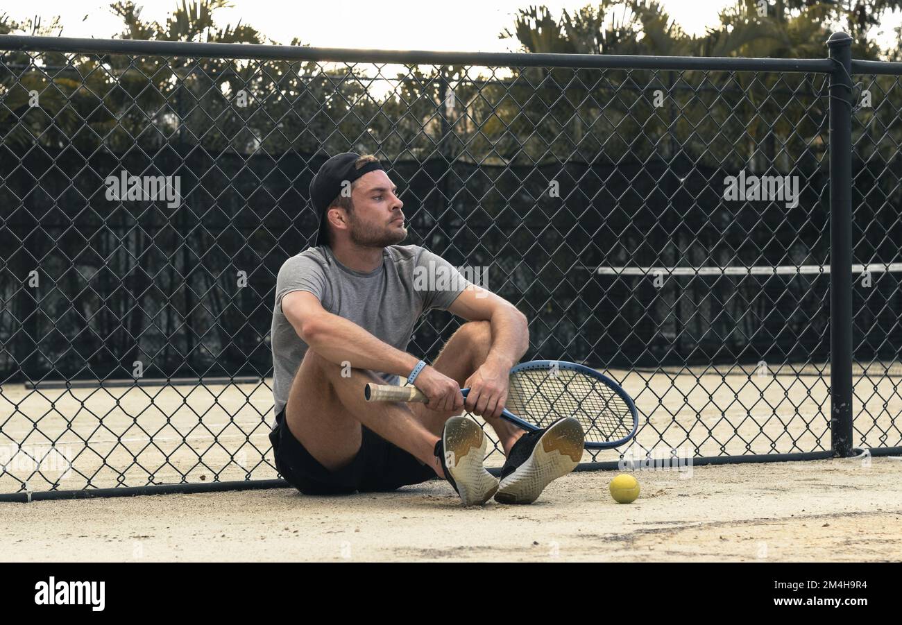 Uomo tennista seduto sul campo da tennis e in attesa del suo turno per giocare a tennis. Foto Stock