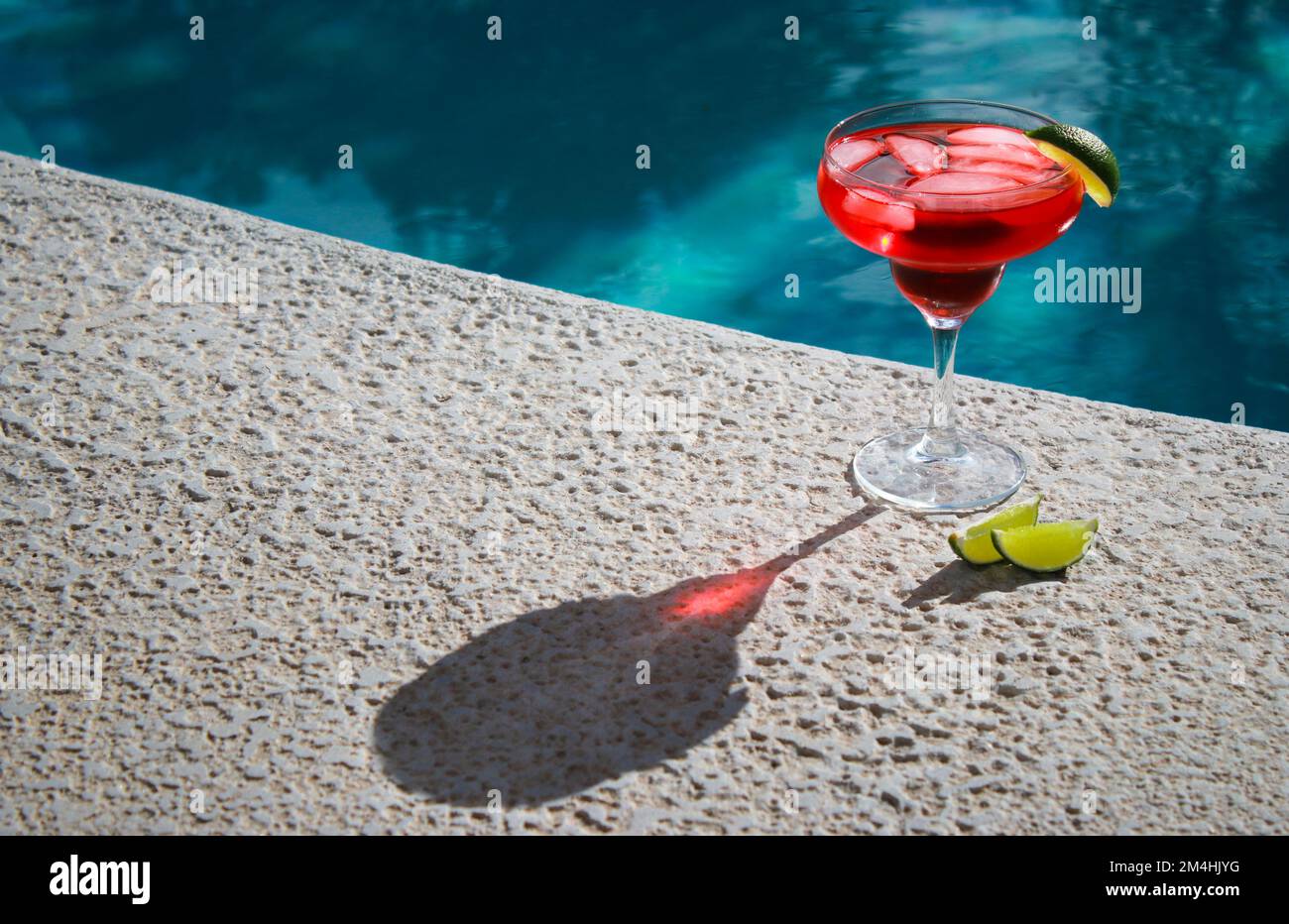Primo piano di cocktail rosso rinfrescante con lime verdi in piscina Foto Stock