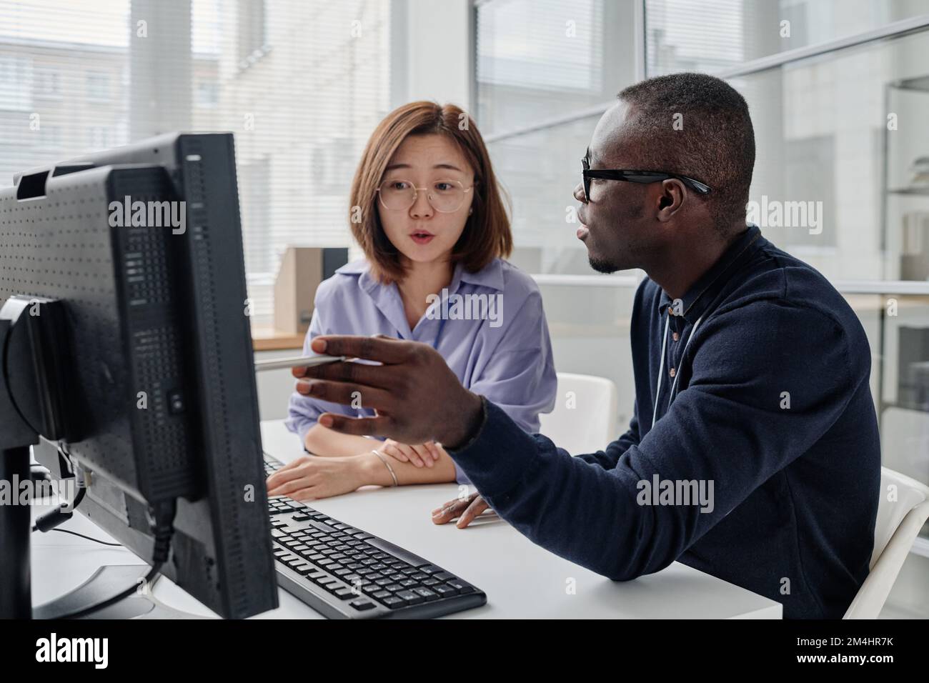 Programmatore afro-americano che punta al monitor del computer e discute il programma del computer con il suo collega Foto Stock