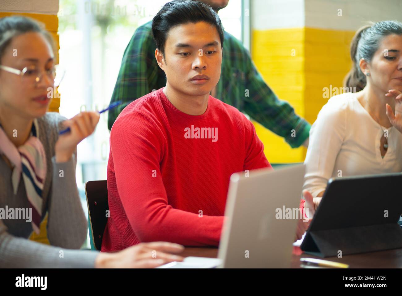 Un gruppo di persone che lavorano insieme come team su un progetto in uno spazio di lavoro congiunto. Persone multirazziali. Guardando il laptop davanti a loro sul woo Foto Stock