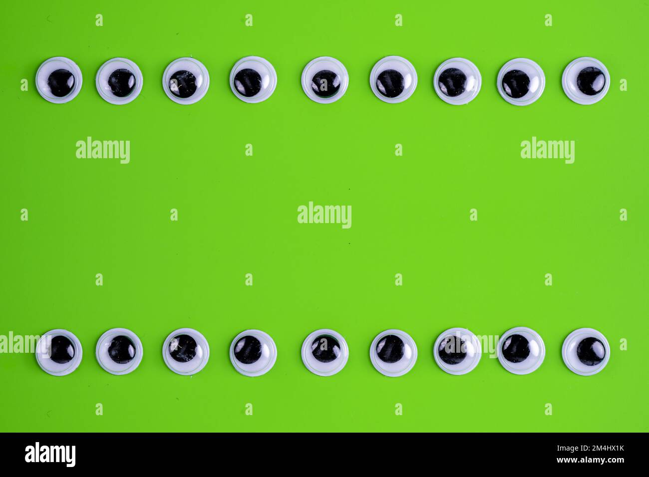 fondo verde lime con due file di occhi googly per formare una cornice Foto Stock