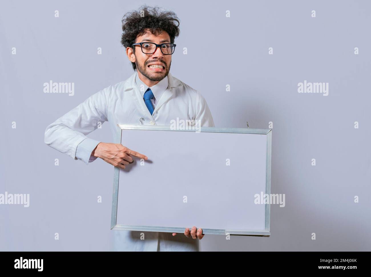 Uomo stupito in cappotto bianco che indica una lavagna bianca. Scienziato maschile in cappotto bianco che tiene e indica una lavagna bianca. Uomo dai capelli disheveled Foto Stock