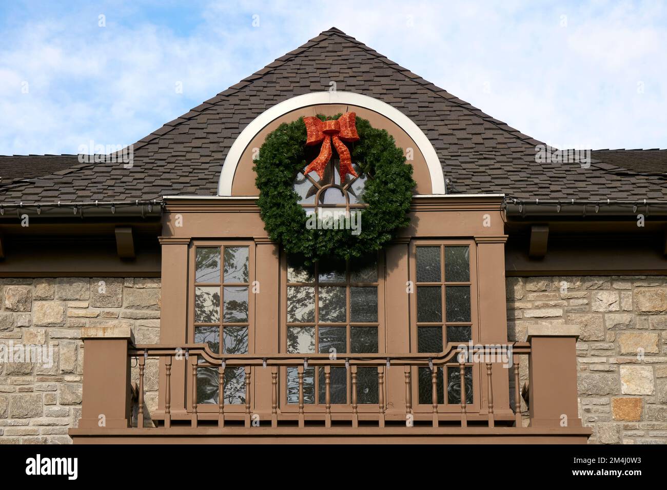 Grande corona di Natale verde tradizionale con arco rosso che decorano la parte anteriore di una casa Foto Stock