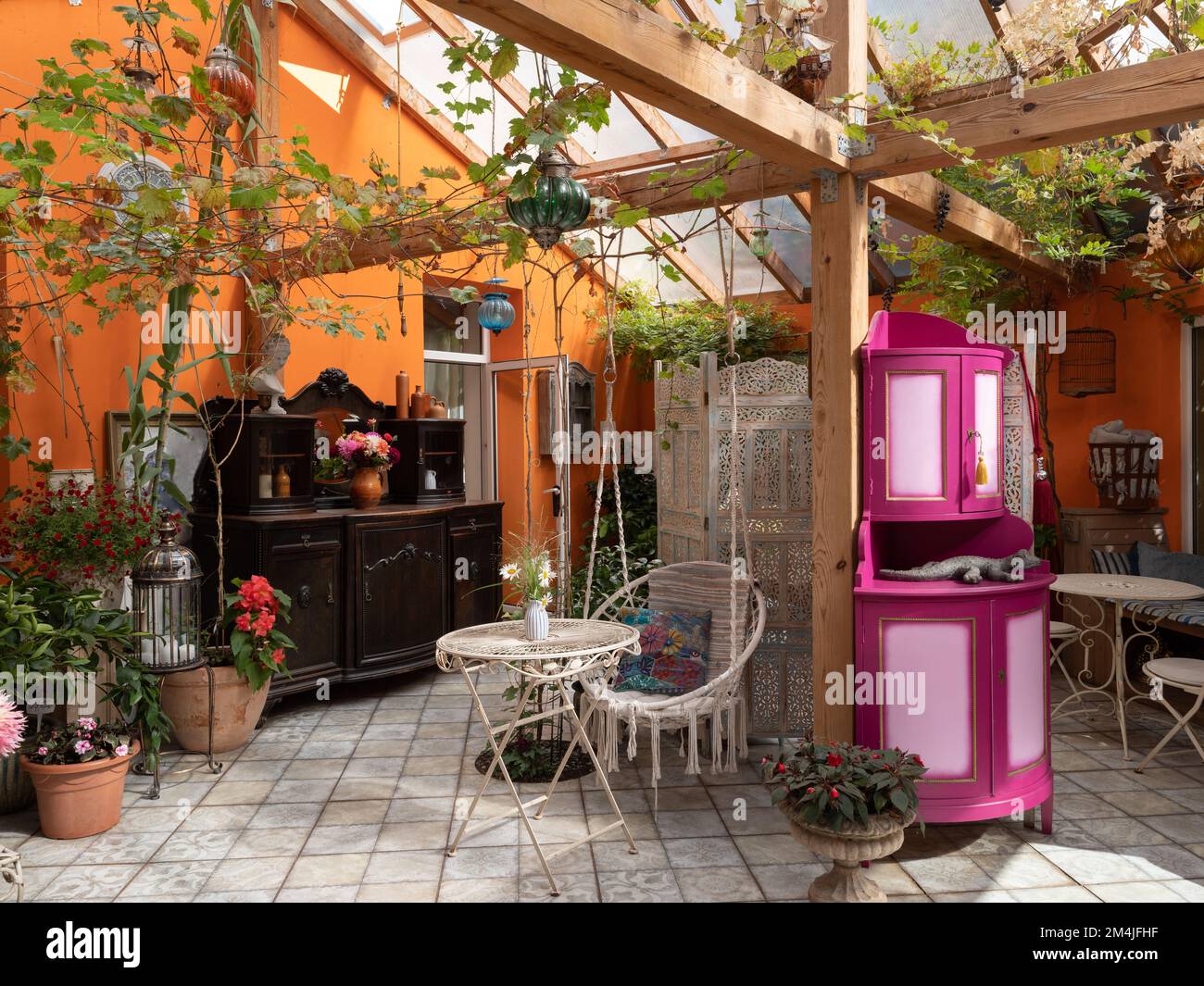 Interno di veranda. Mobili in legno. Sedia sospesa in vimini, piante. Foto Stock