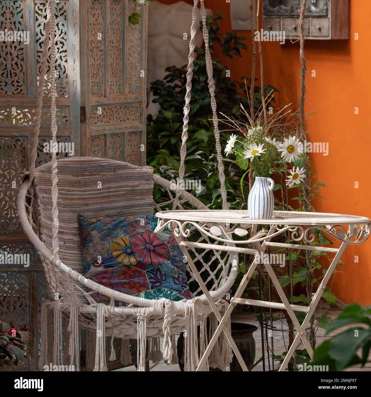 Interno di veranda. Sedia sospesa in vimini, fiori sul tavolo. Primo piano. Foto Stock