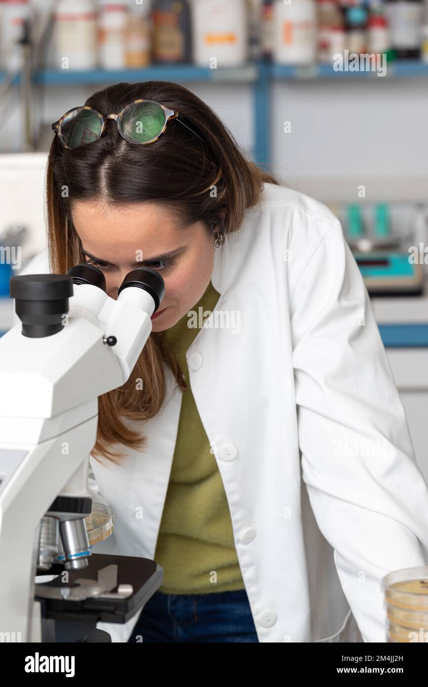 Giovane scienziata donna sotto un microscopio in un laboratorio scientifico. Concetto di ricerca per le malattie rare ed eccellenza scientifica. Biologo durante un Foto Stock
