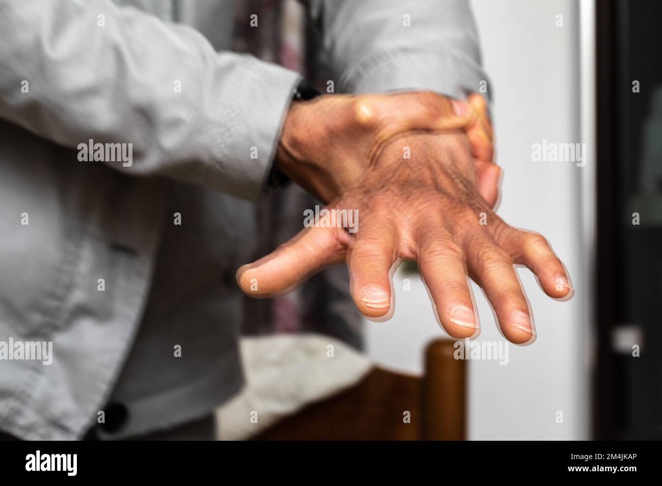 Macro di una mano caucasica anziana con tremori. Effetto sfocato di una doppia esposizione. Concetto di paziente di malattia di Parkinson che cerca di calmare il tremito della mano Foto Stock