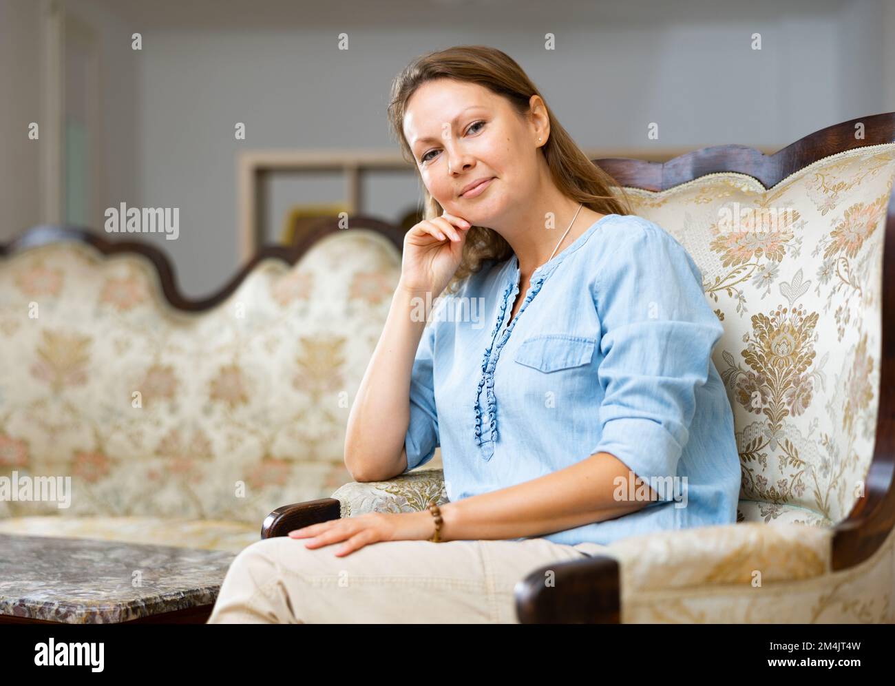 Donna elegante di mezza età in una blusa blu seduta sul divano e guardando  la macchina fotografica in accogliente appartamento Foto stock - Alamy