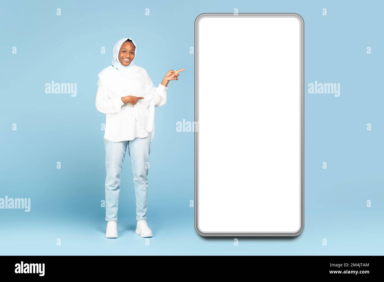 Ottima offerta. Tutta la lunghezza del corpo di donna nera felice in hijab che punta al grande display vuoto dello smartphone, mockup Foto Stock