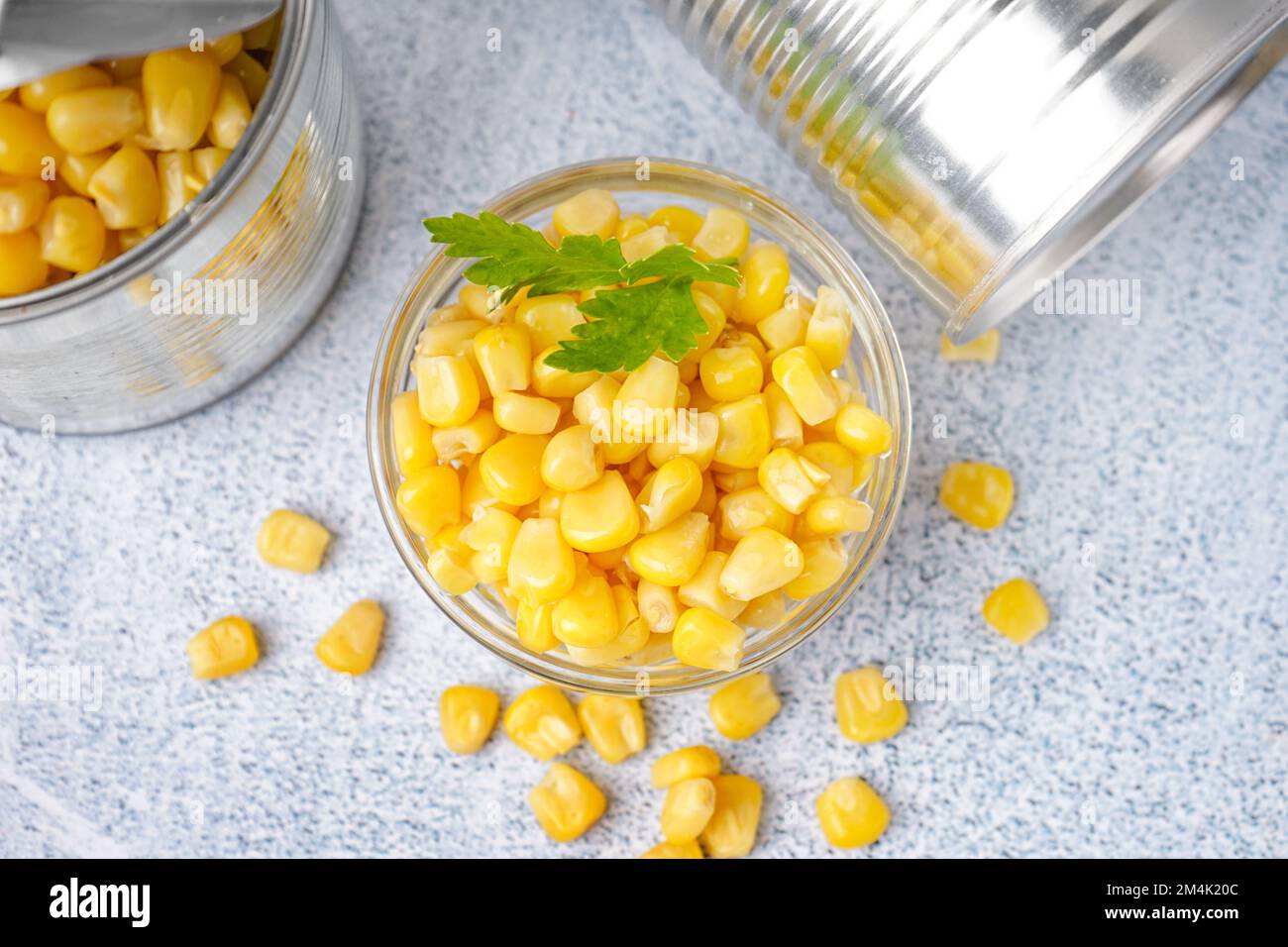 Lattine, ciotola con semi di mais e foglia di prezzemolo sul tavolo grigio Foto Stock