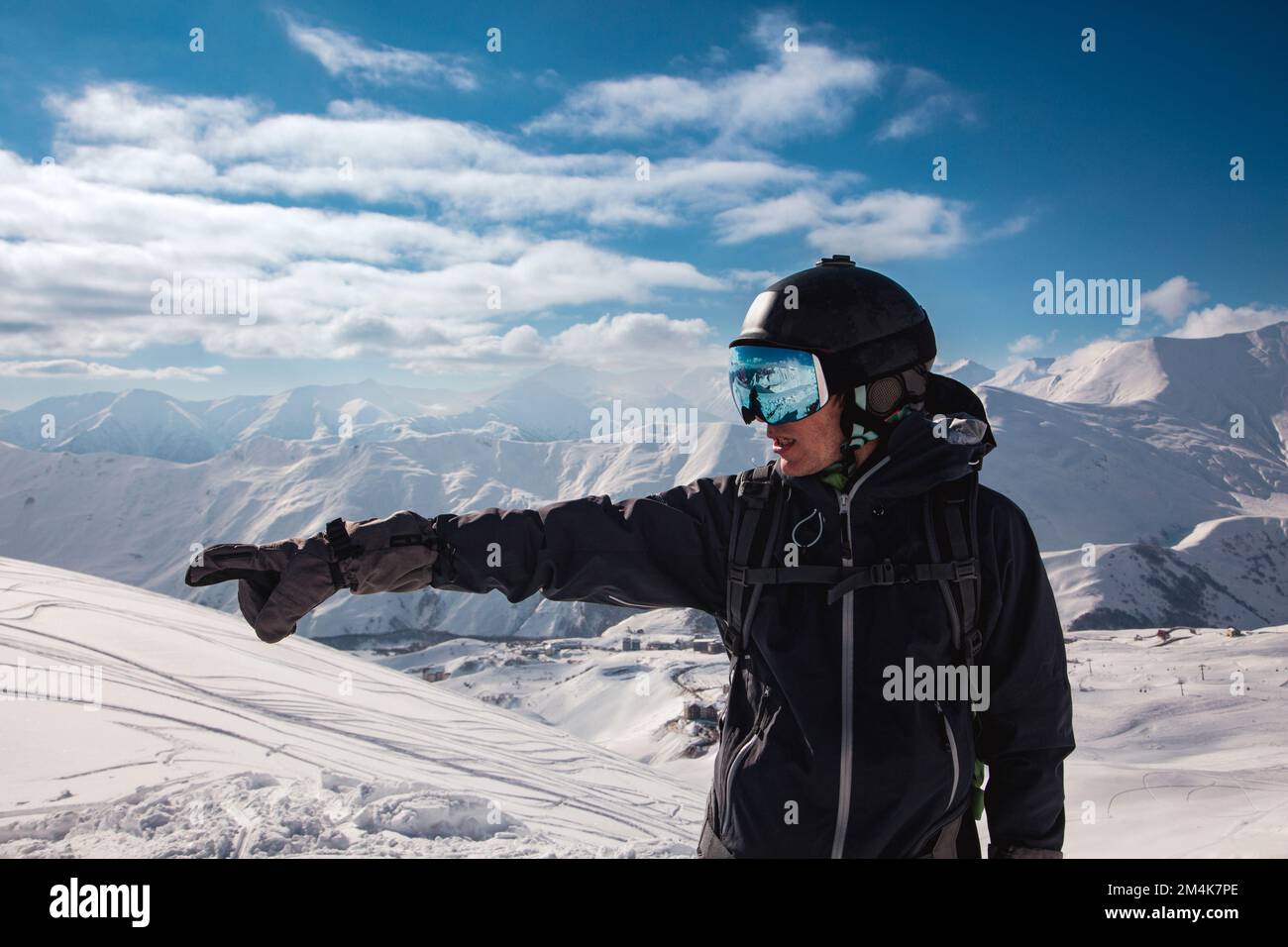 Un viaggiatore in una maschera da sci punta a sinistra verso le alte montagne del Caucaso, sport estremo freeride invernale Foto Stock