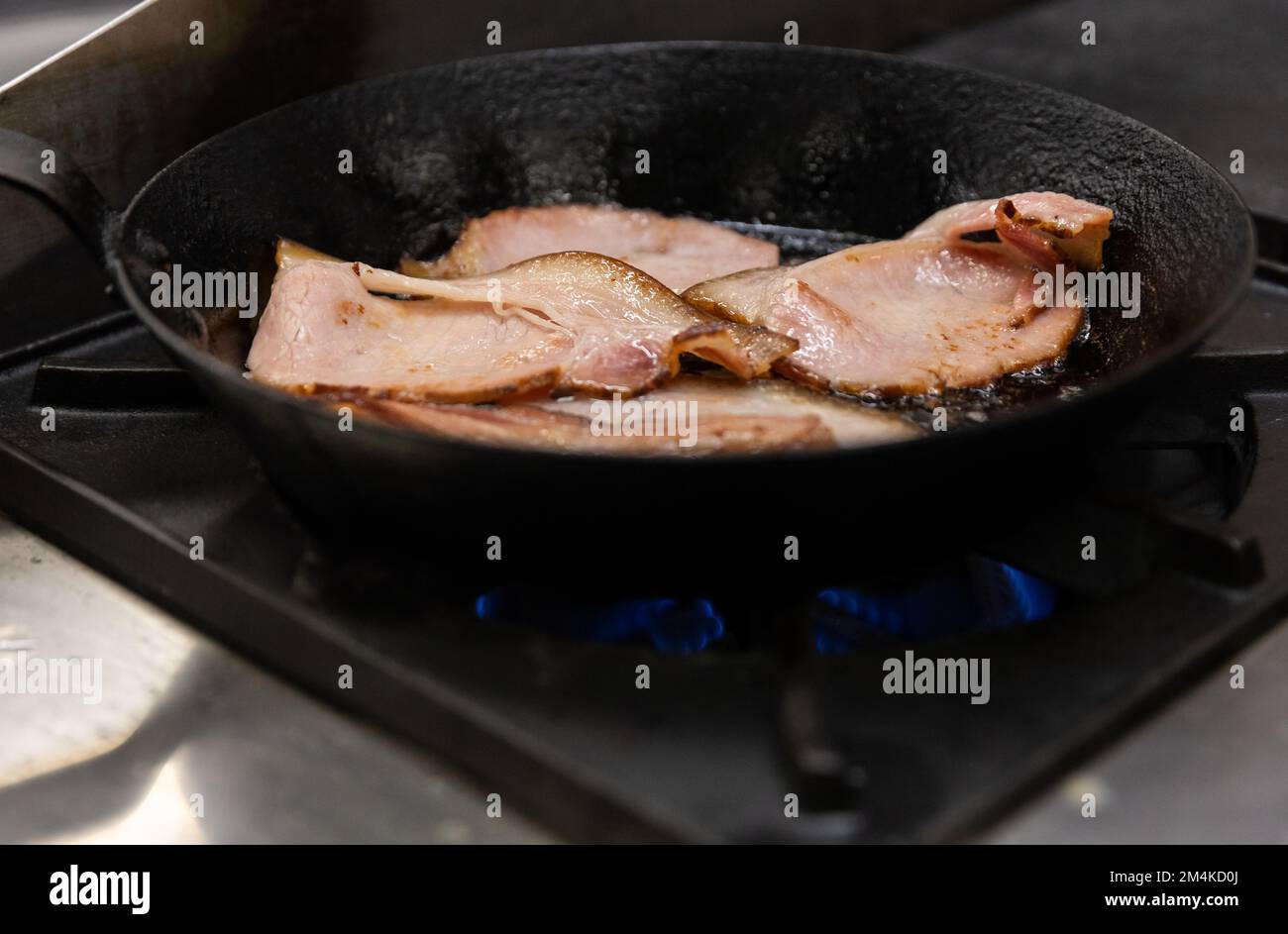 Fettine di pancetta tagliate a fette spesse che friggono in una padella di ghisa Foto Stock