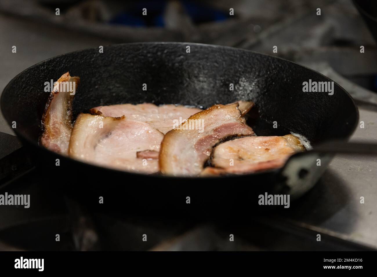 Fettine di pancetta tagliate a fette spesse che friggono in una padella di ghisa Foto Stock