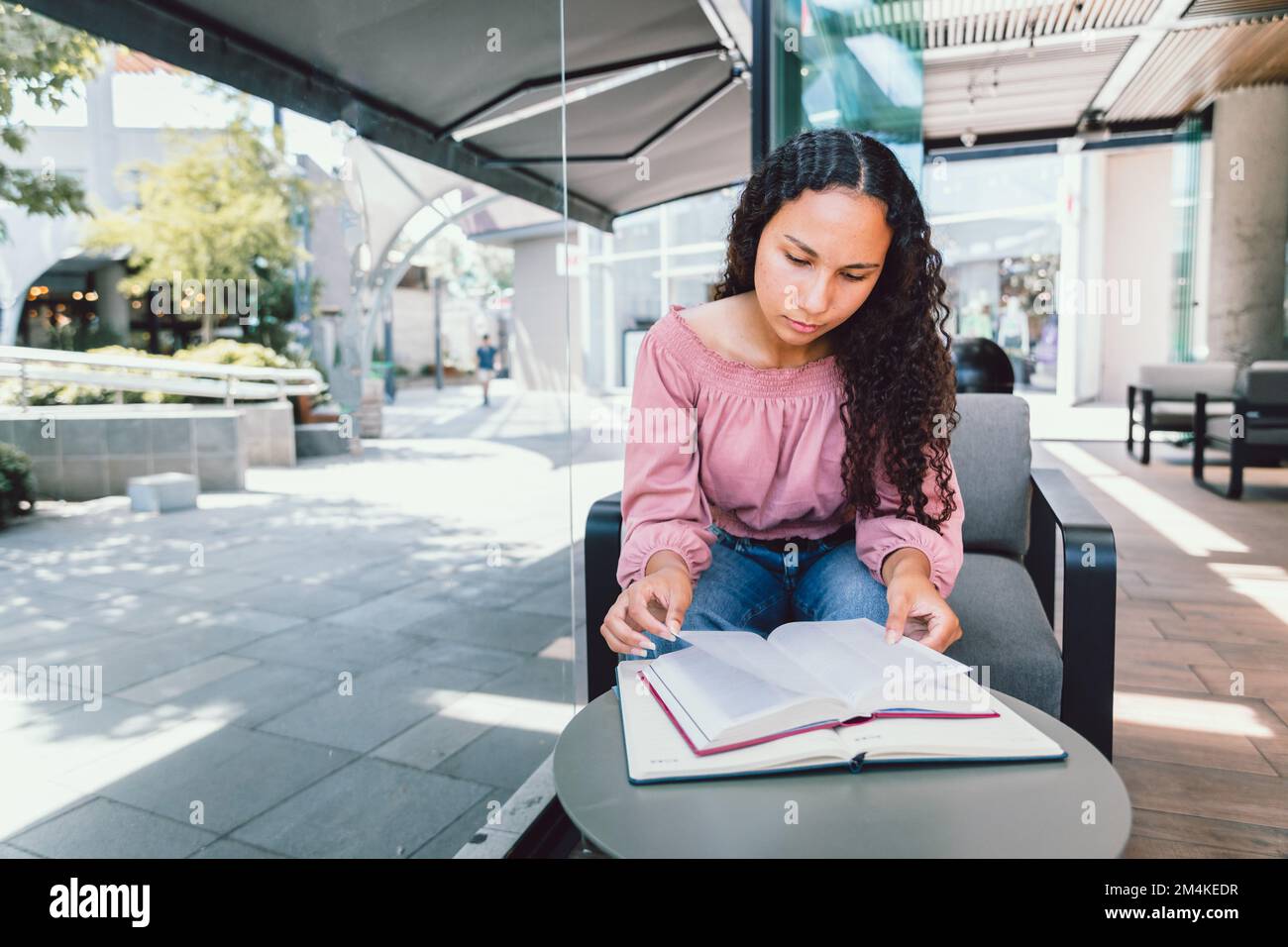Studentessa universitaria latina seduta e studentessa per un esame al di fuori di un bar. Leggere libri Foto Stock