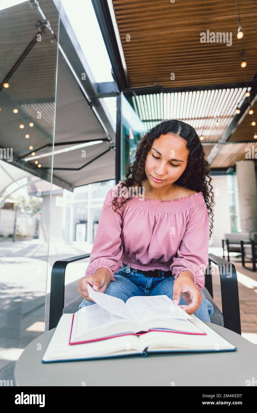 Studentessa universitaria ispanica seduta e studio per un esame fuori da un bar. Leggere libri Foto Stock