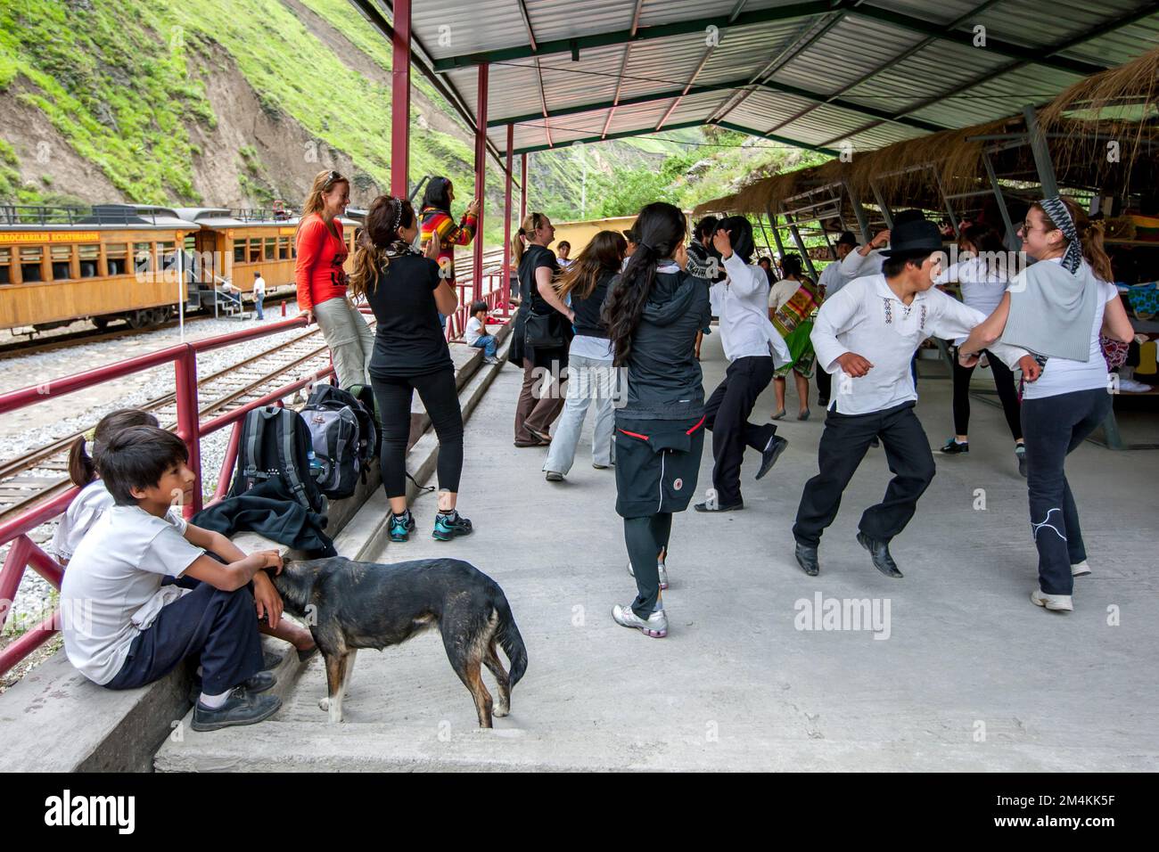 Turisti e uomini ecuadoriani ballano alla Stazione di Sibambe in Ecuador dopo aver cavalcato la ferrovia a zig-zag del naso del Diavolo da Alausi. Foto Stock