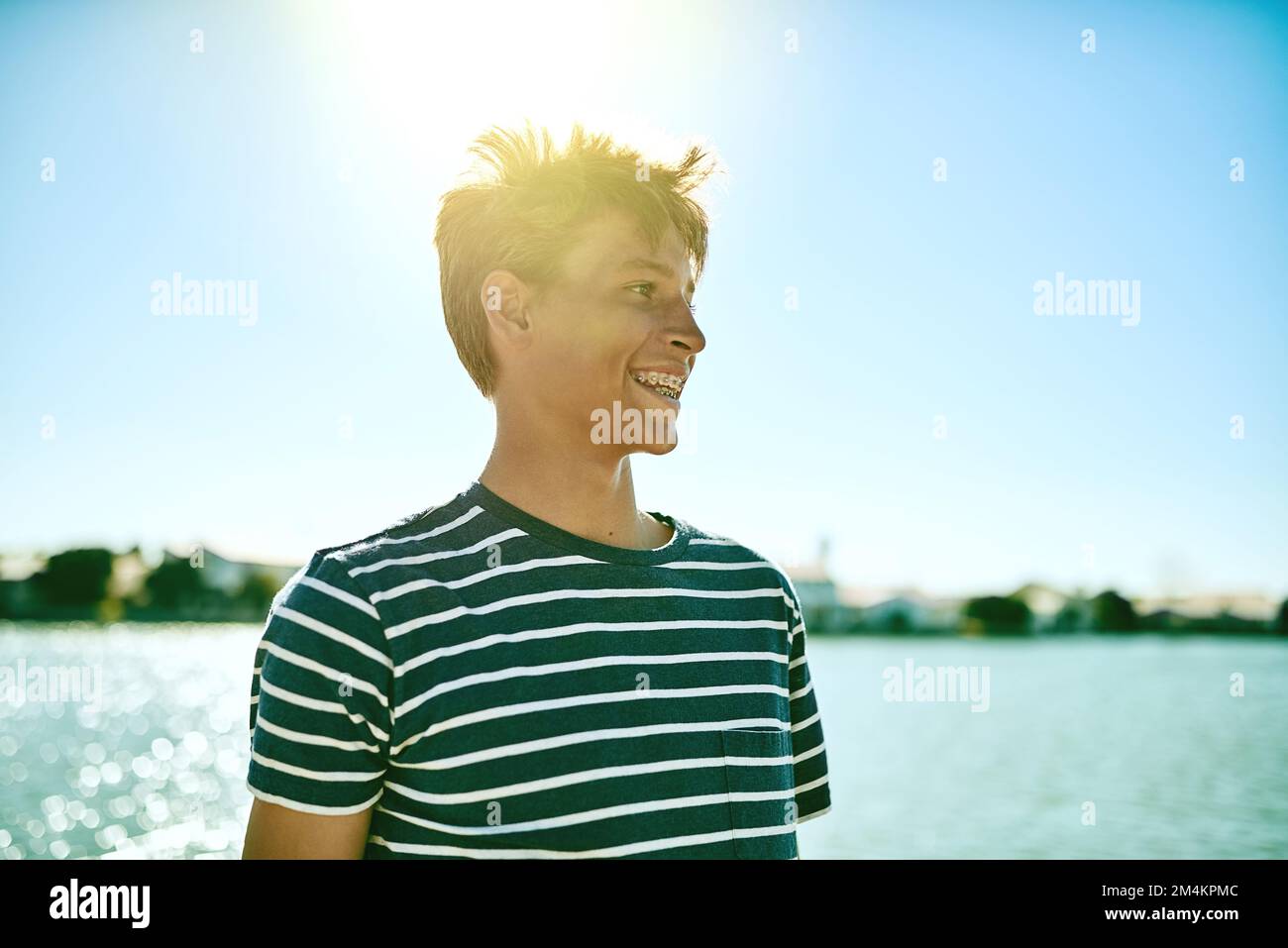 Ama stare al sole. un giovane ragazzo in piedi fuori con una laguna sullo sfondo. Foto Stock