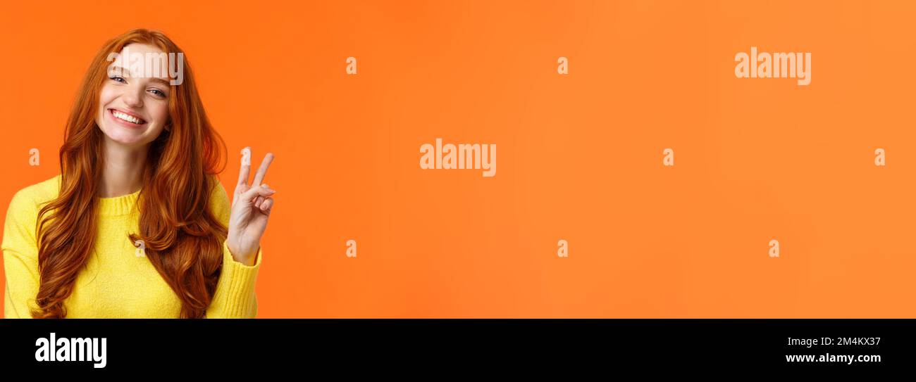 Girovita allegra splendida donna rossa con lunghi capelli ricci rossi, che mostra segno di pace e sorridente felice, positività espressa, come le vacanze invernali Foto Stock