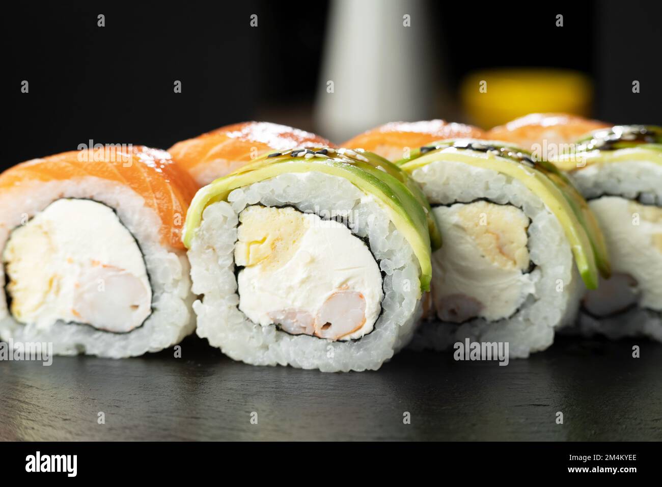 Rotolo di sushi Philadelphia con gamberi, avocado e salmone su sfondo nero con riflessione. Primo piano. Menu sushi. Cucina giapponese Foto Stock