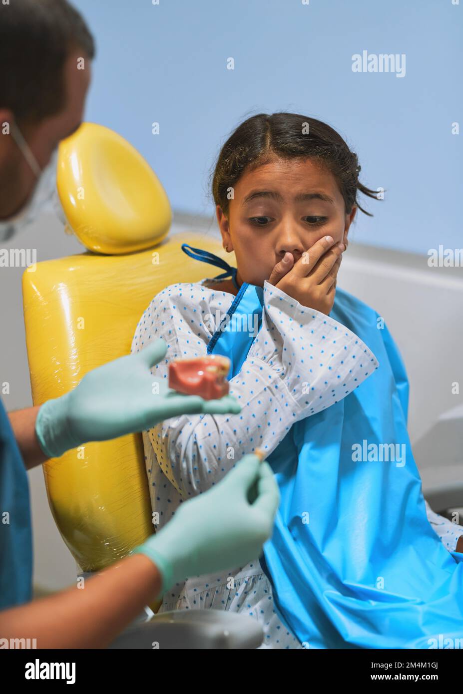 WOW non ho mai saputo che assomiglia così. una bambina che guarda sorpresa tenendo chiusa la bocca mentre guarda un dente che il dentista ha appena tirato Foto Stock