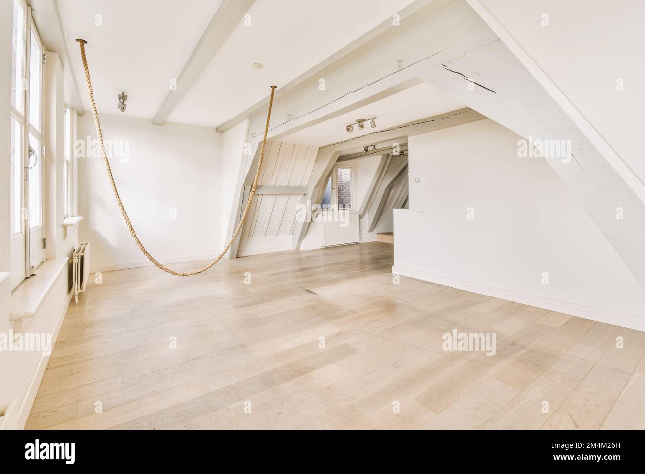 una stanza vuota con pareti bianche e pavimento in legno su un lato, c'è una corda sospesa dal soffitto all'altro Foto Stock