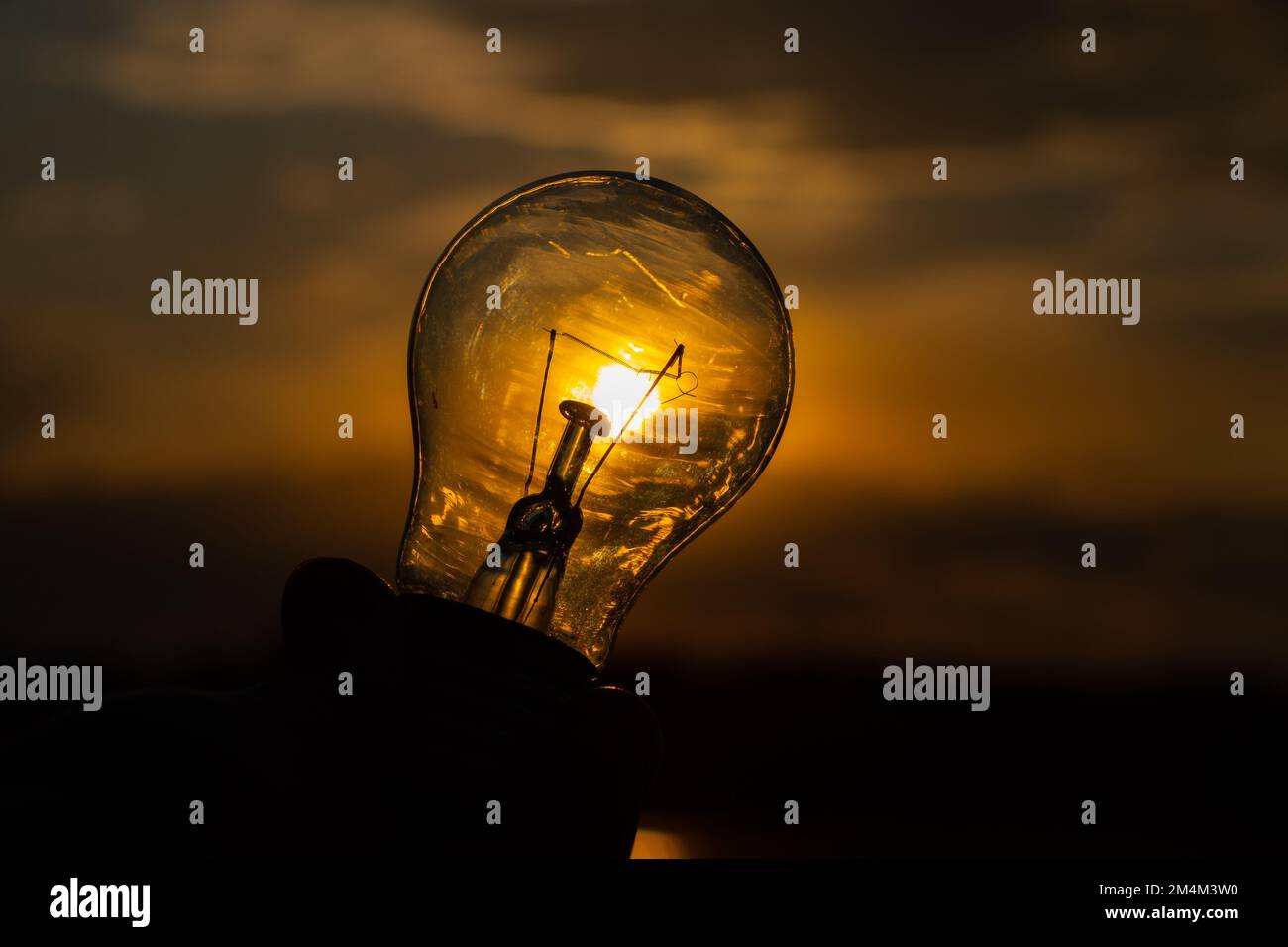 lampadina a incandescenza in mano su sfondo tramonto primo piano Foto Stock