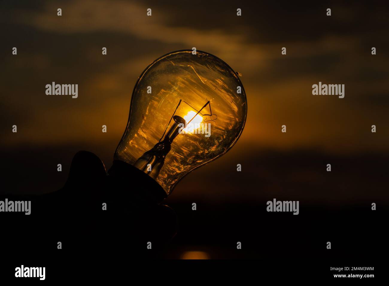 lampadina a incandescenza in mano su sfondo tramonto primo piano Foto Stock