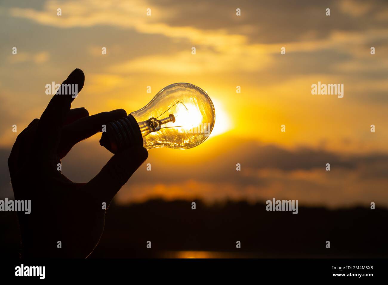 lampadina a incandescenza in mano su sfondo tramonto primo piano Foto Stock