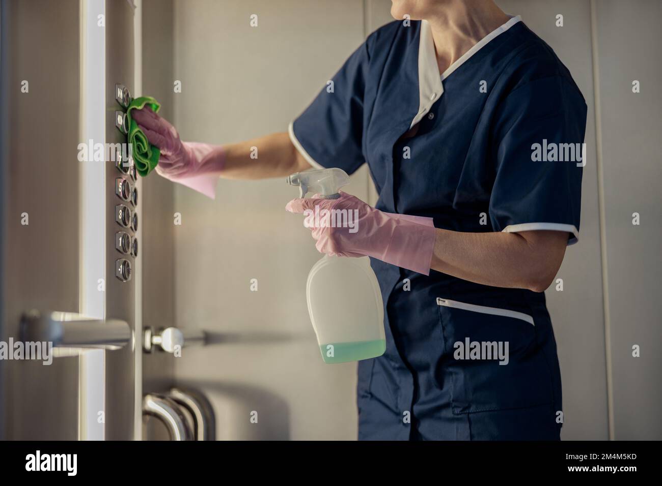 Primo piano della cameriera che indossa uniforme e guanti pulizia ascensore con detergente e straccio Foto Stock