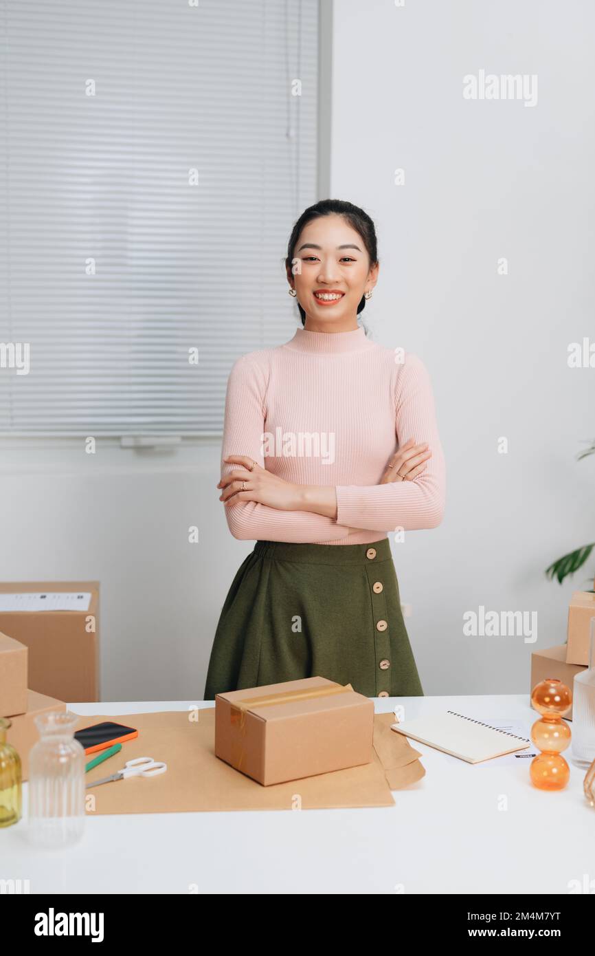 ragazza proprietario in piedi sicuro con le braccia incrociate preparare ordine inviare al cliente imballaggio scatola per la consegna, lavorando online a casa Foto Stock